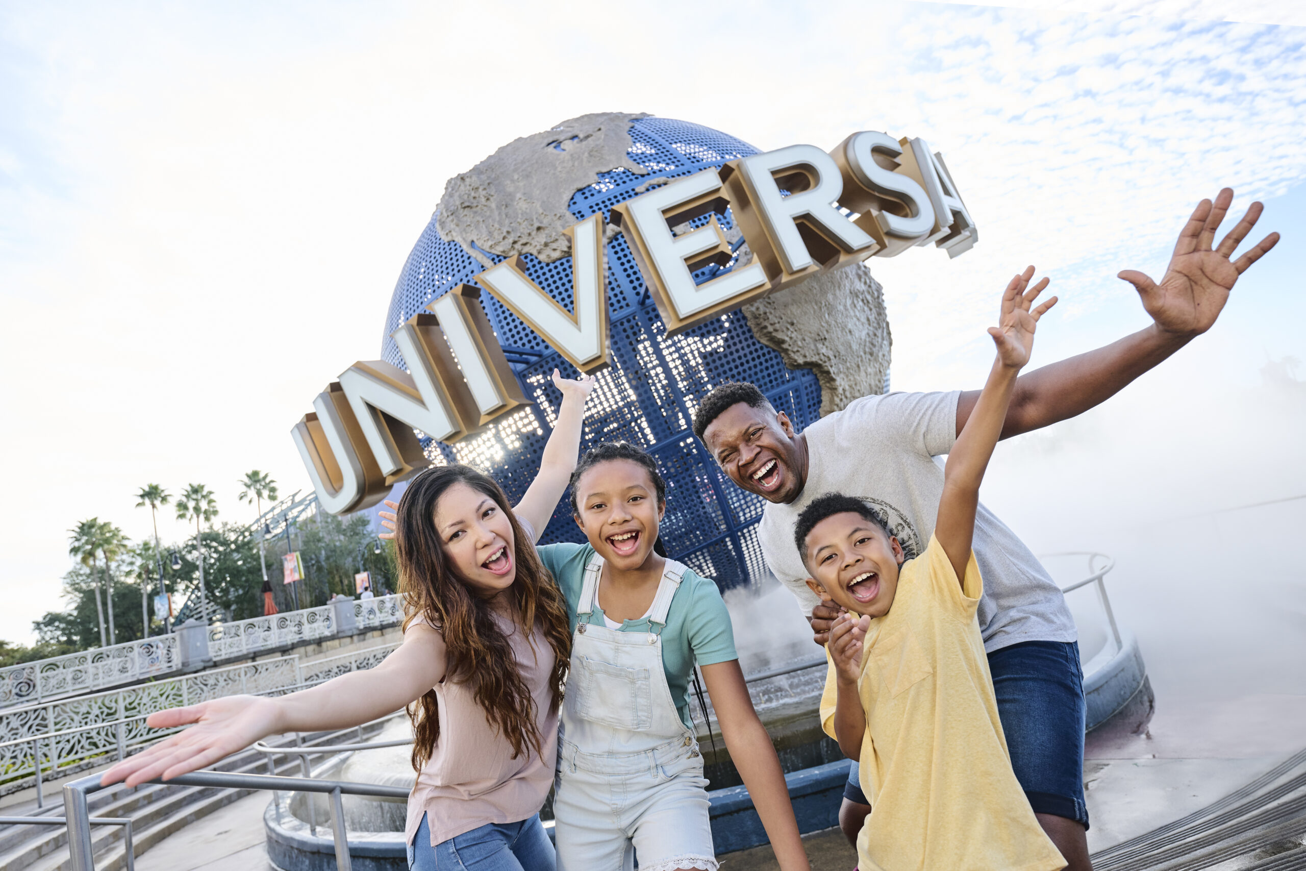 a family of 4 stands in a laughing pose with arms outstretched in front of the Universal Globe