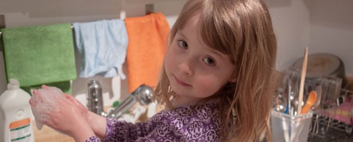 A young girl washing her hands in the kitchen sink.