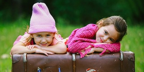 Two girls laying their heads on their arms while they pose on a trunk outside.